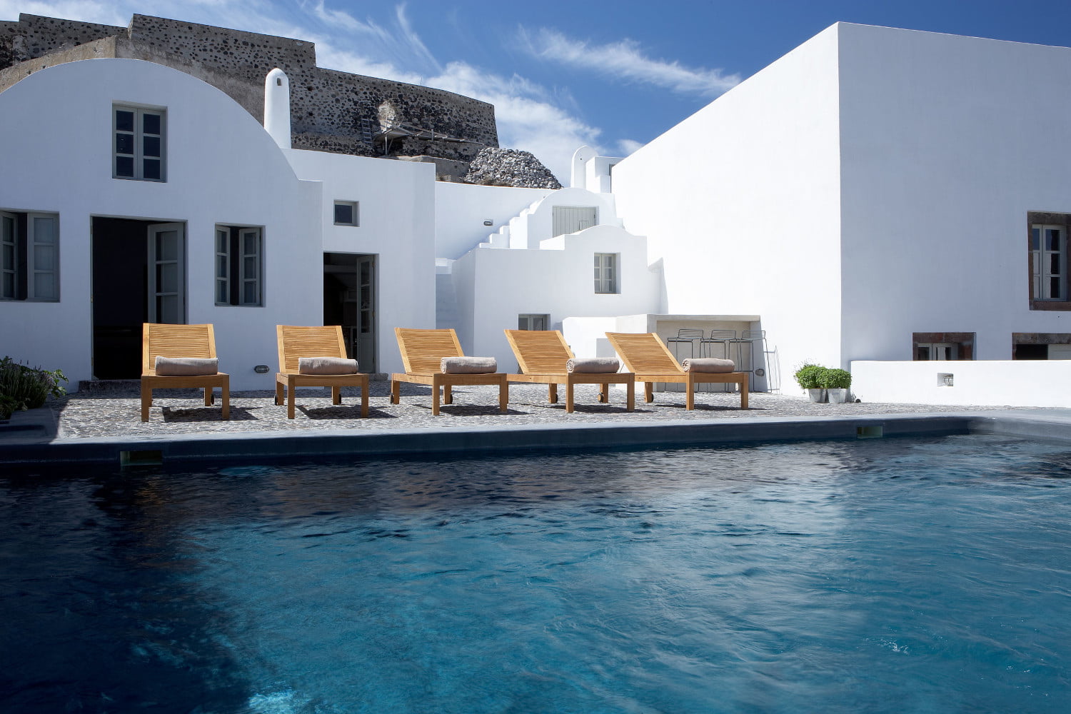 Main pool with counter-current swimming at the Villa Lucia in Pyrgos Santorini Greece by Rent A Greek Villa. in the backdrop is the building facade, a exterior pool and the wall of the remaining Venetian Castle ``Kasteli``