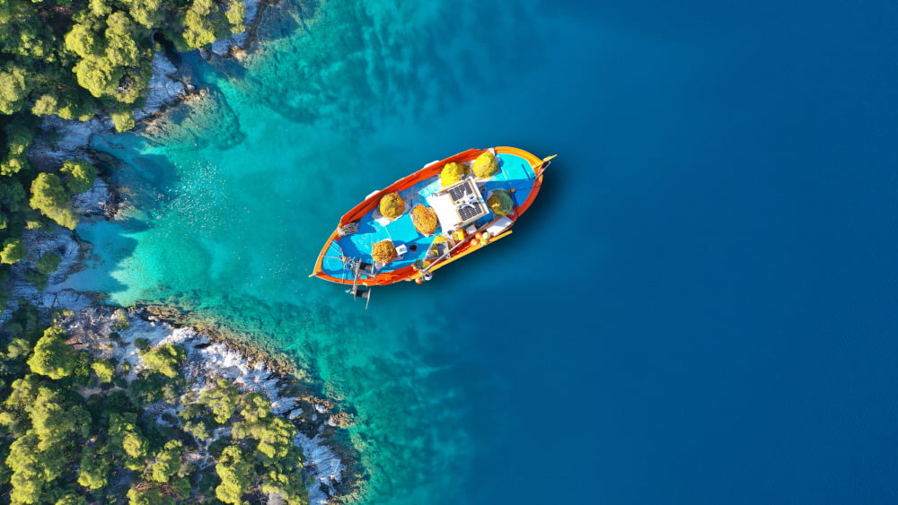 Destinaation Alonissos Sporades island complex feauring a traditional Greek fishing boat in a secluded cove with clear turquoise waters and pine forested reaching the sea by RentAGreekVilla powered by PathTravelDesigns Greece