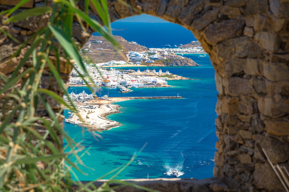 Destination Mykonos Town view through a window on a stone wall by RentAGreekVilla powered by PathTravelDesigns Greece