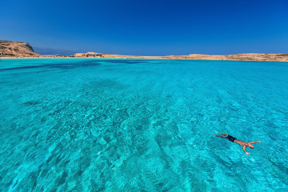 A man swimming in the turquoise blue waters of Koufonisia in Pori Bay by RentAGreekVilla PathTravelDesigns