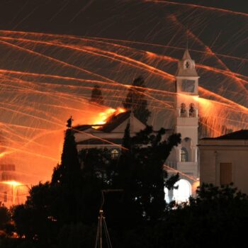 Chios rocket wars | Easter in Greece A white church bell tower at night and rockets flying in the air. This is part of a list of unique local Greek customs for celebrating a traditional Easter in Chios Greece