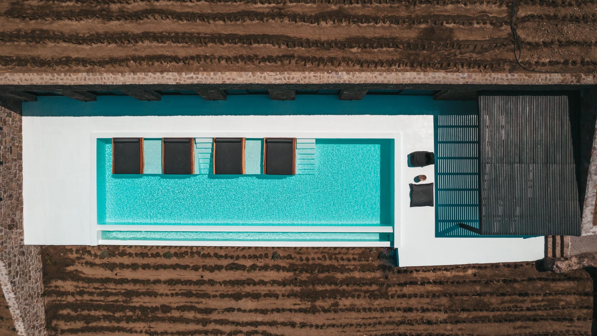 the pool of Villa Romelia with its black sunbeds as seen from above in Mykonos with a complete guide on how to choose a luxury villa for your holidays