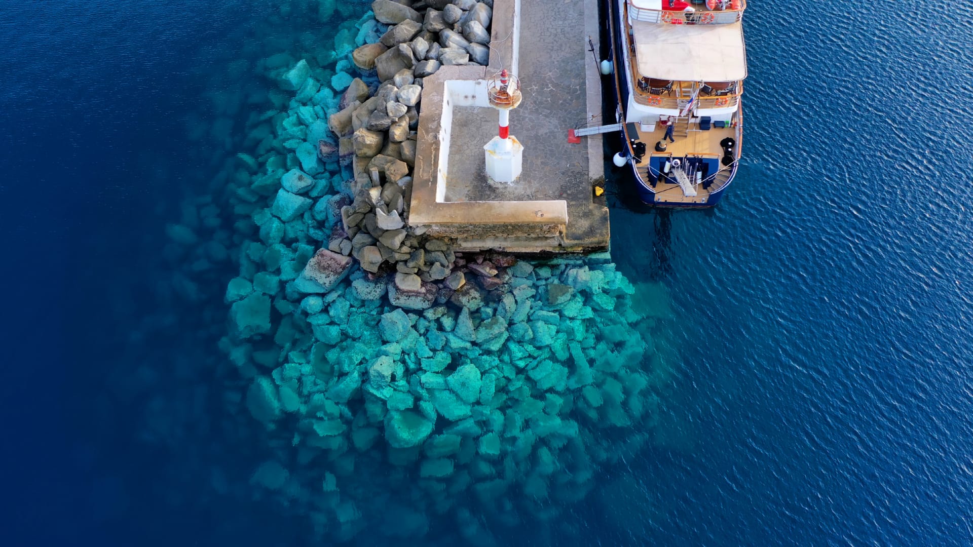 A boat as seen from above while docked in the harbour of Mykonos as this how travellers visit the Cyclades while island hopping in Greece.