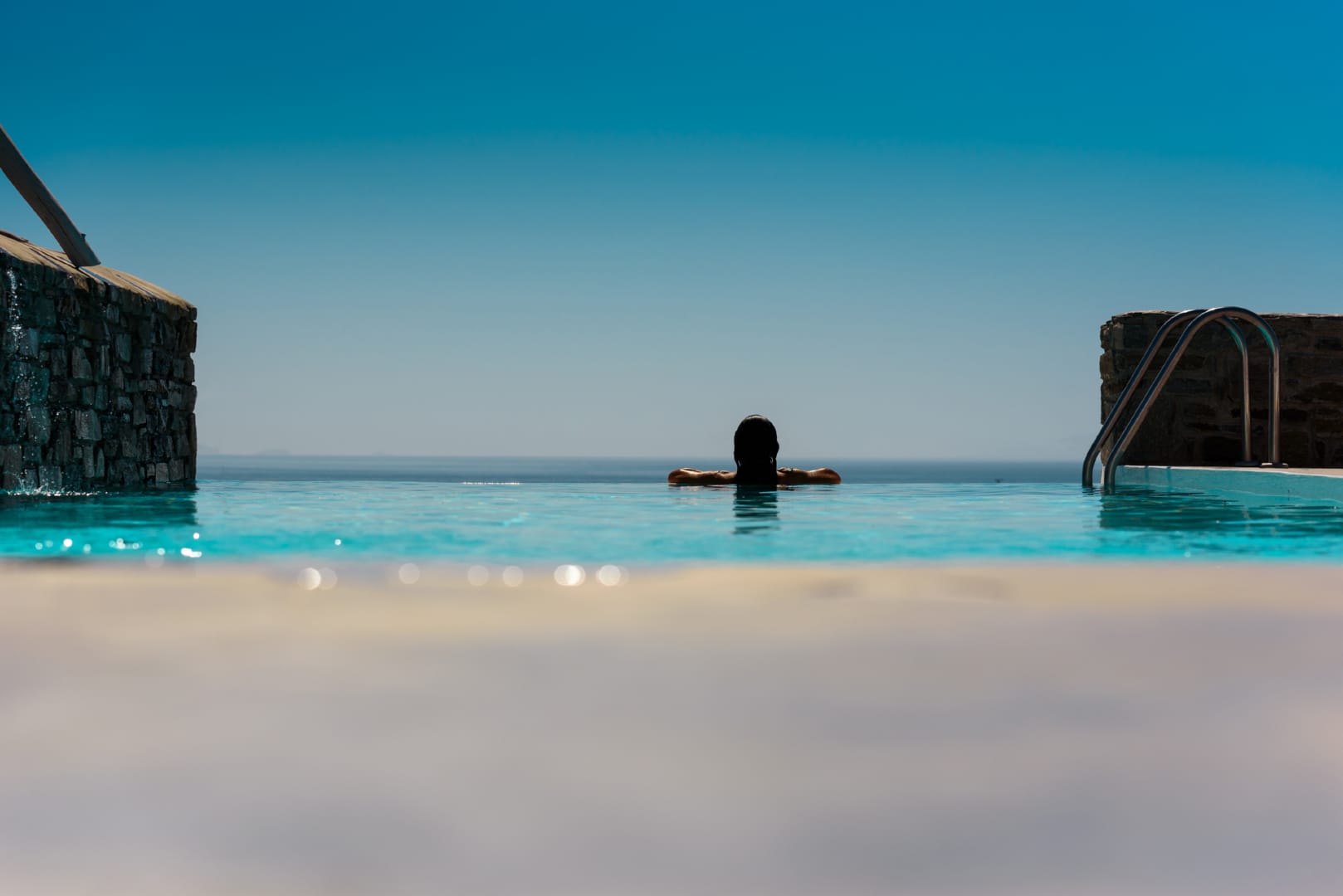 A woman in the infinity pool of the rental Villa Palia in Paros looking out to the Aegean Sea.