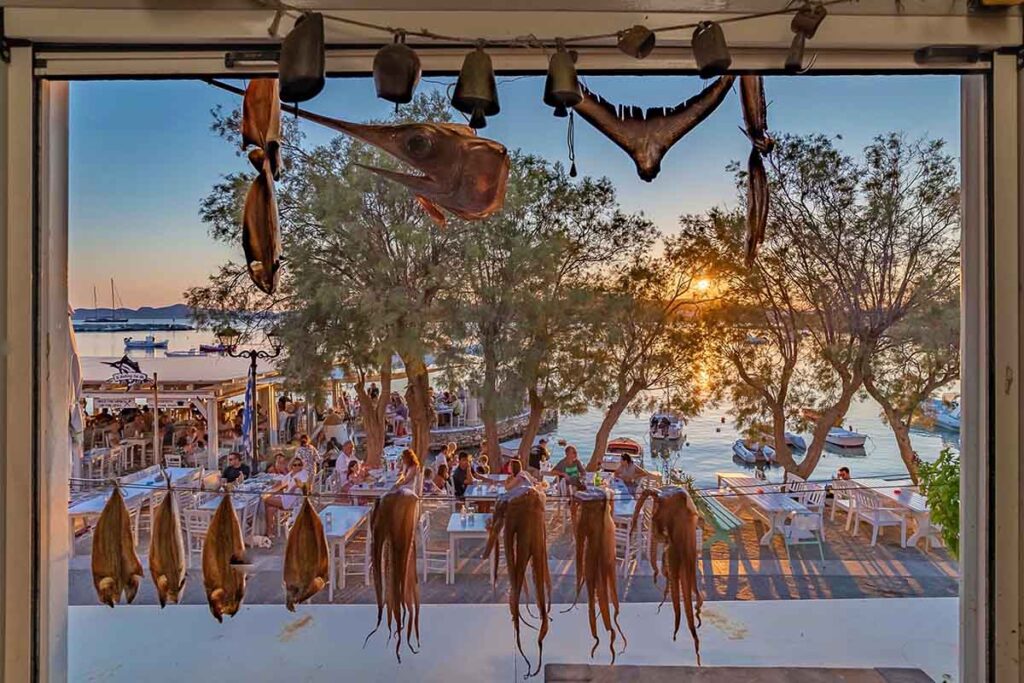 Paros Food Guide | Where To Eat In Paros by Rent A Greek Villa Looking out through the window to the dining area by the sea in Paros, from one of the restaurant found in the food guide where to eat on the island by Rent A Greek Villa